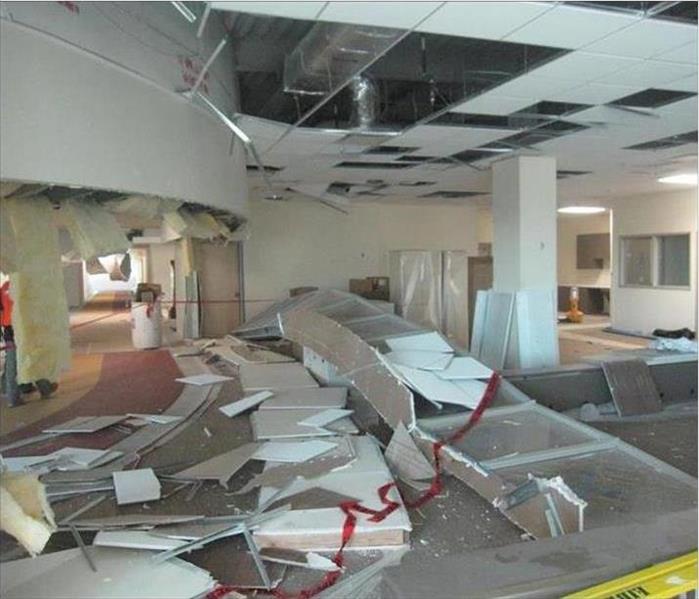 An office area where ceiling tiles, insulation, and cubicle walls are scattered on the floor; holes in the ceiling 