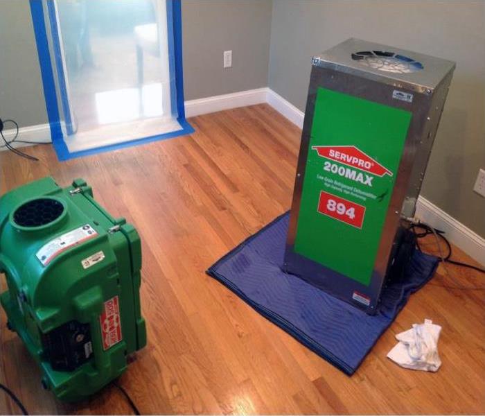 An air scrubber and dehumidifier in a bed room with wood floors. The doorway is covered by a containment barrier.