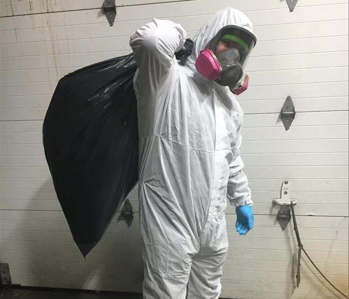 Technician in full personal protective equipment carrying wet insulation in a trash bag